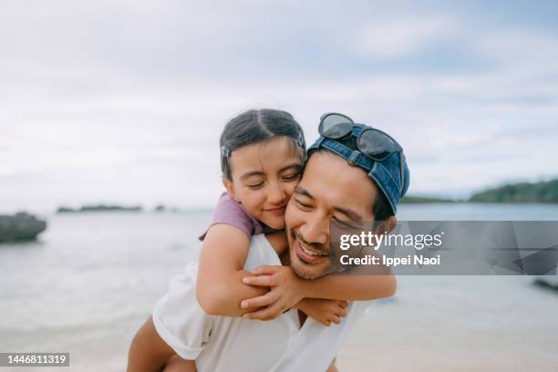 father giving piggyback ride to young daughter on beach - portrait candid ストックフォトと画像