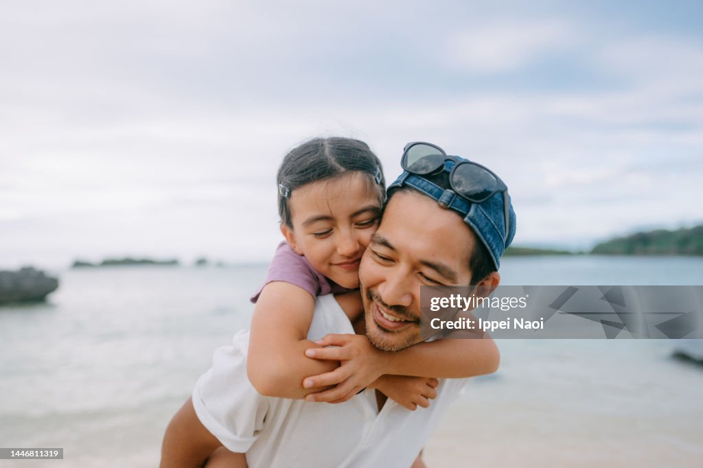 Father giving piggyback ride to young daughter on beach