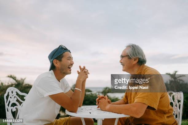 senior father and adult son chatting on patio - familia de dos generaciones fotografías e imágenes de stock