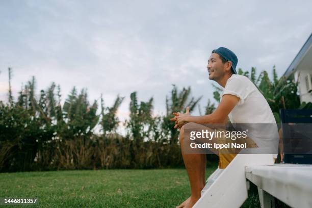 man sitting on porch and looking at view with smile - asian man seated stockfoto's en -beelden