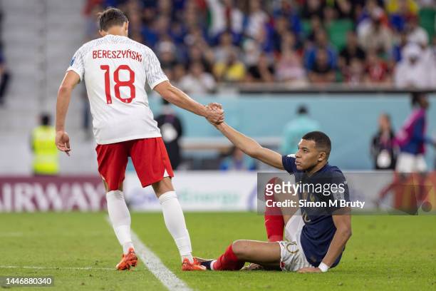 Kylian Mbappe of France is helped off the ground by Bartosz Bereszynski of Poland during the FIFA World Cup Qatar 2022 Round of 16 match between...