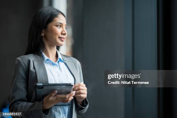 cash flow planning can improve your finances for the future. side view of an asian female financial advisor working in a modern business office holding a tablet computer while looking through a window. - trusted business advisor foto e immagini stock