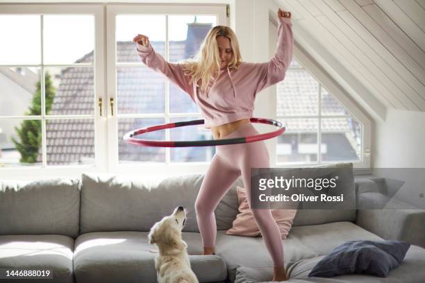young woman using plastic hoop on sofa at home watched by her dog - pivot stock pictures, royalty-free photos & images