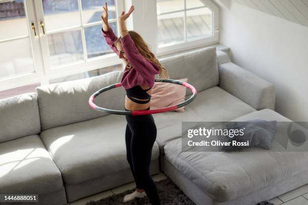 young woman using plastic hoop in living room at home - gymnastikreifen stock-fotos und bilder