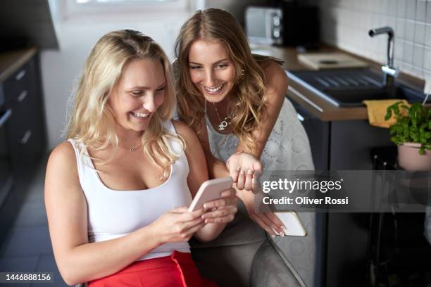 two happy female friends at home sharing mobile phone - good news stock pictures, royalty-free photos & images