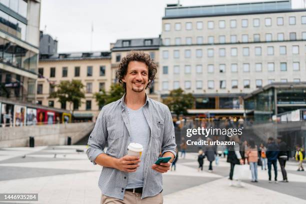 young man using phone and drinking coffee in stockholm - sergels torg imagens e fotografias de stock