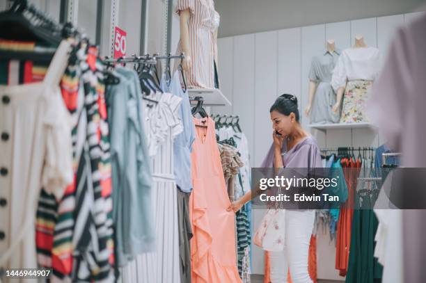 asian indian female talking on the phone while shopping in a clothing store looking for new dress - womenswear 個照片及圖片檔