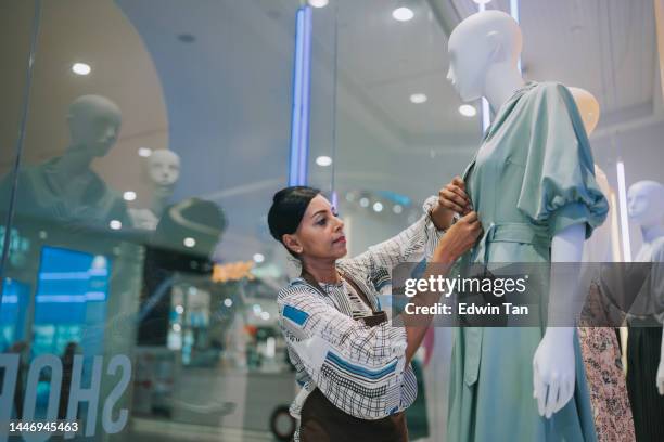 asian indian women display artist dressing up mannequin in store window display at womenswear clothing store - clothing store stock pictures, royalty-free photos & images