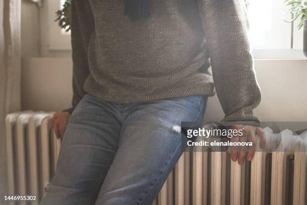mature adult man warms himself by the radiator in the room - climate grief stock pictures, royalty-free photos & images