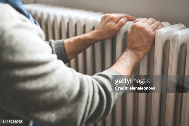 mature adult man warms himself by the radiator in the room - electric fire stock pictures, royalty-free photos & images