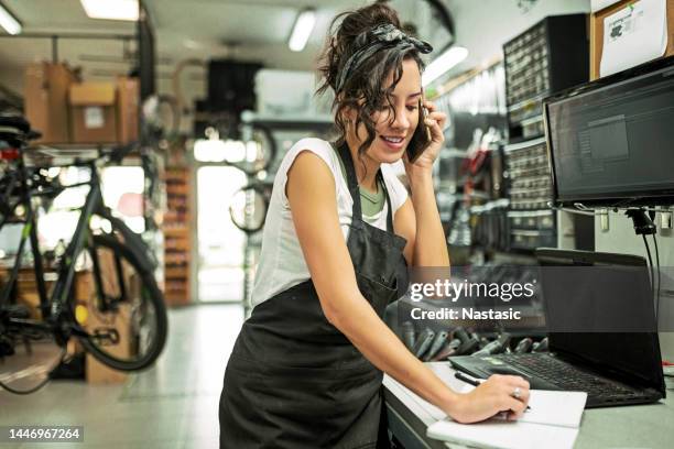 hermosa joven mecánica de bicicletas hablando con un cliente usando el teléfono - emprendedor fotografías e imágenes de stock