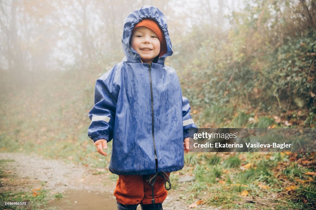 Portrait of a smiling child 2-3 years old in a blue raincoat walking in the rain in nature