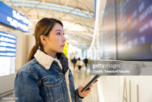 asian woman checking boarding time on time table screen before boarding in the airport - incheon airport ストックフォトと画像