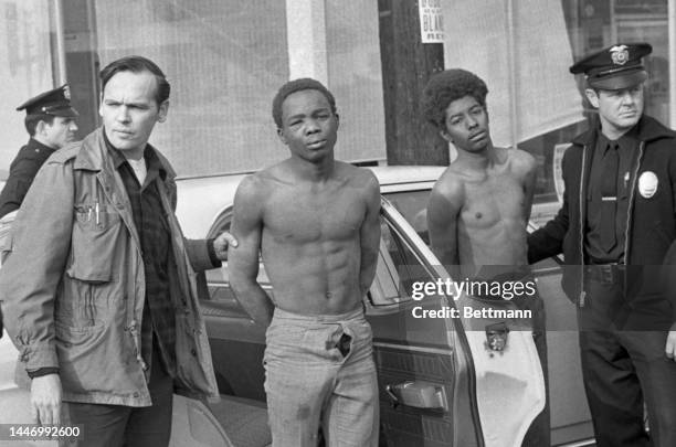 Police officers hold two members of the Black Panthers that were arrested after police laid siege to the party headquarters. Three police officers...