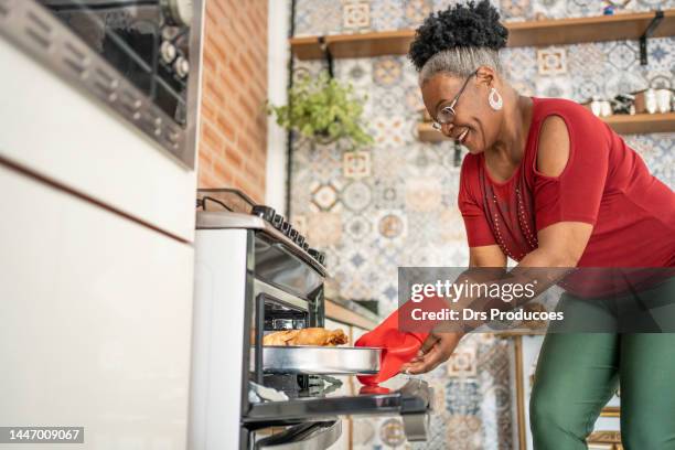 mature woman taking christmas turkey out of the oven - chicken roasting oven stock pictures, royalty-free photos & images