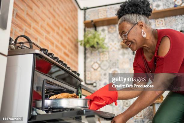une femme mûre sort la dinde de noël du four - gant de cuisine photos et images de collection