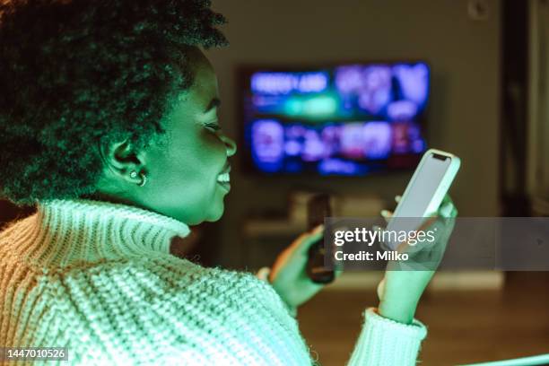 young woman holding smart phone and tv remote control - glee tv program stockfoto's en -beelden