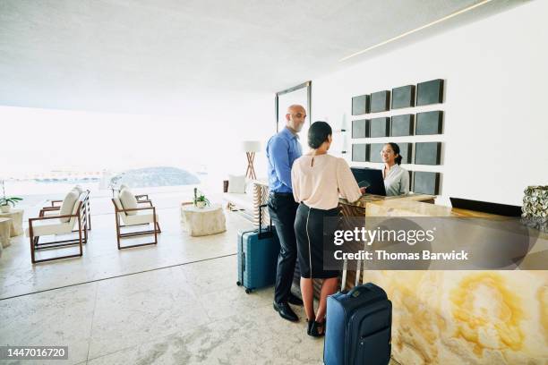 wide shot of business colleagues checking into hotel at front desk - reception hotel photos et images de collection