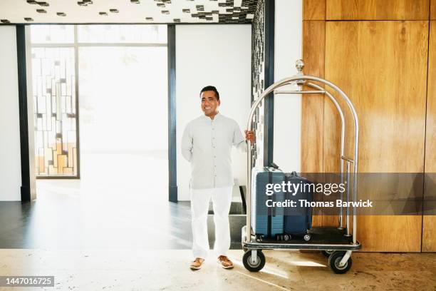 wide shot of bellman standing with luggage cart at hotel entrance - luggage trolley stockfoto's en -beelden
