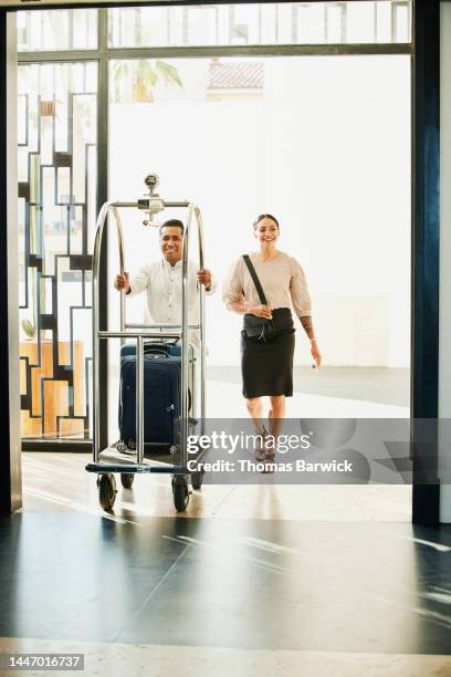 wide shot of bellman helping businesswoman with luggage at hotel - bell hop stock pictures, royalty-free photos & images