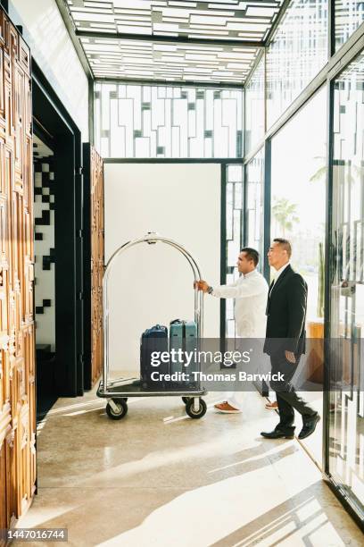 wide shot of bellman helping businessman with luggage at hotel - bellhop stock pictures, royalty-free photos & images