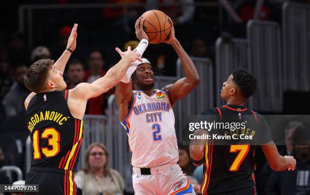 Shai Gilgeous-Alexander of the Oklahoma City Thunder turns the ball over as he is defended by Bogdan Bogdanovic and Jarrett Culver of the Atlanta...