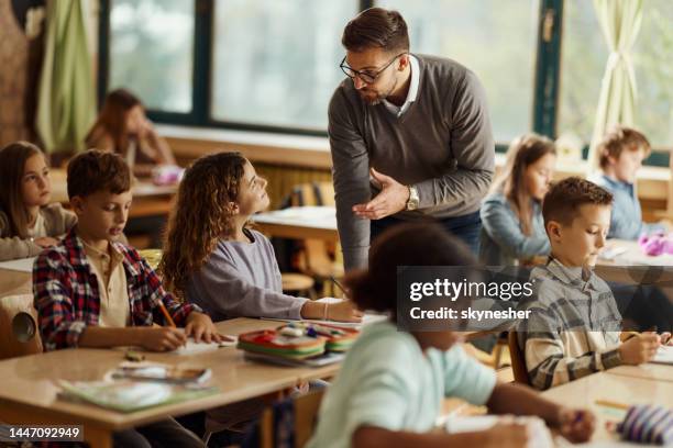 männlicher lehrer, der einem schulmädchen im klassenzimmer assistiert. - male teacher in a classroom stock-fotos und bilder