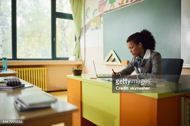 african american teacher writing her plans in the classroom. - grading stock pictures, royalty-free photos & images