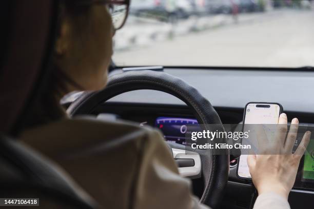 over the shoulder view of woman using gps navigation app on smartphone in a car - mobile app car stock pictures, royalty-free photos & images