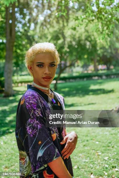 portrait of a teenage transgender boy in a colorful shirt in a park. looking at camera - genderblend stock-fotos und bilder