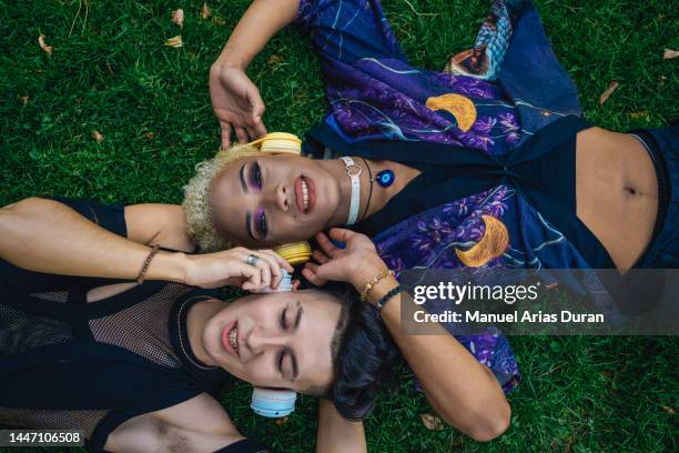 we all love music. high angle of a couple of gay friends lying on their backs on the grass in a park and listening to music. - street style in madrid stock pictures, royalty-free photos & images