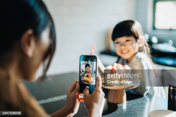 cropped shot of young asian mother celebrating 5th birthday with her lovely daughter, taking pictures with smartphone of the birthday girl holding a number 5 candle in front of the birthday cake. birthday celebration and party theme - chinese family taking photo at home stock pictures, royalty-free photos & images