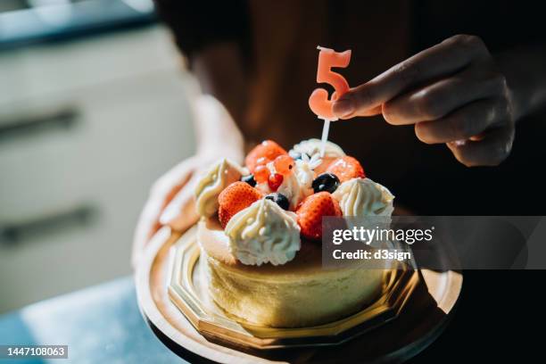 close up of a woman's hand putting a candle on birthday cake. hands of a mother putting a number 5 candle on birthday cake to celebrate her little daughter's 5th birthday. birthday celebration and party theme - cheesecake fotografías e imágenes de stock