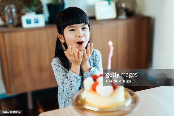 Portrait of a happy 5 years old Asian girl showing excitement with her birthday cake, singing birthday song and making a wish on her birthday. Birthday celebration and party theme