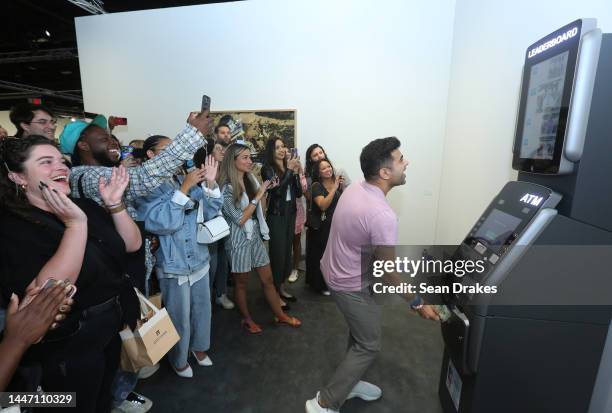 Sajan Patel receives $20 dollars from an ATM Leaderboard installation presented by Perrotin during Art Basel Miami Beach in the Miami Beach...