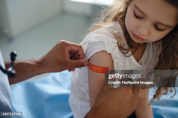 young doctor giving plaster strip to little girl after vaccination. - childhood vaccinations stock pictures, royalty-free photos & images
