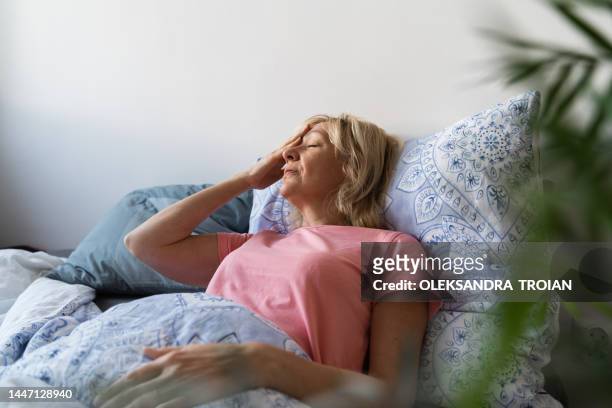 middle aged woman having hot flashes in bed - hot flash stock pictures, royalty-free photos & images