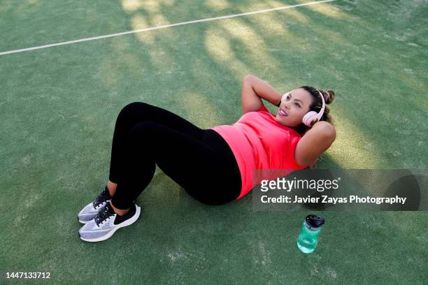 plus size latin woman doing sit-ups after jogging - sit ups stockfoto's en -beelden