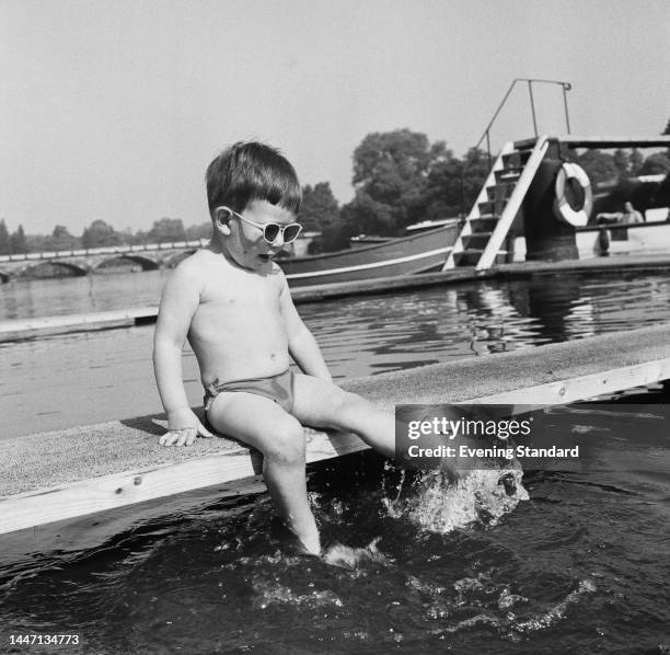 Young boy in swimming trunks and sunglasses splashing the water with his feet at the Serpentine Lido in London's Hyde Park on May 13th, 1961.
