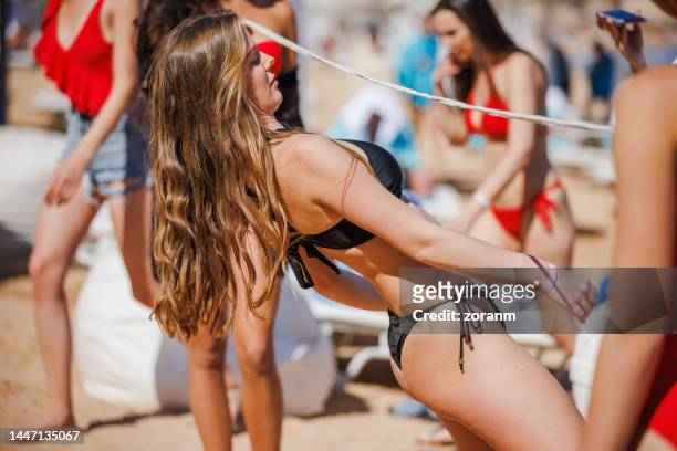 young woman in bikini bending over backwards and sliding under limbo rope on the beach - dance challenge stock pictures, royalty-free photos & images