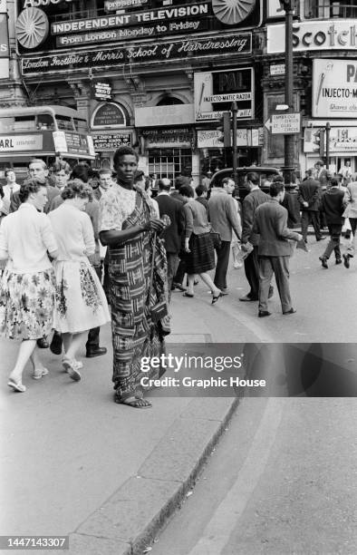 Man wearing traditional African clothing as he stands at the Piccadilly Circus end of Shaftesbury Avenue, as pedestrians walk on the pavement and...