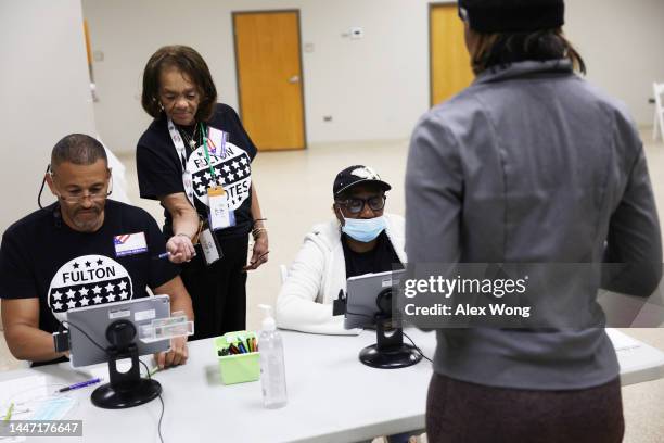 Poll workers help to check a voter in at a polling place during the Senate runoff election on December 6, 2022 in Atlanta, Georgia. Georgians head to...