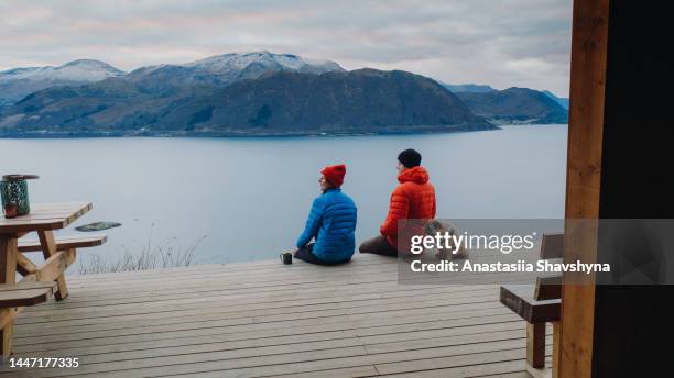 ノルウェーの避難所でリラックスする日没時の風光明媚なフィヨルドの景色を熟考する女性と男性の空撮 - two animals ストックフォトと画像
