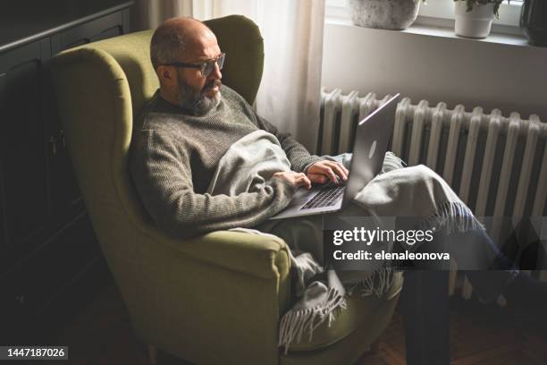 reifer erwachsener mann, der zu hause arbeitet (heizkörper, laptop) - heizung stock-fotos und bilder