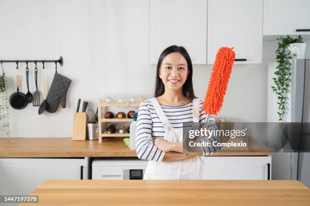 young asian woman looking at camera, cleaning home with duster. beautiful cleaning service worker housekeeping and tidying up the kitchen - huishoudelijke dienstverlening stockfoto's en -beelden