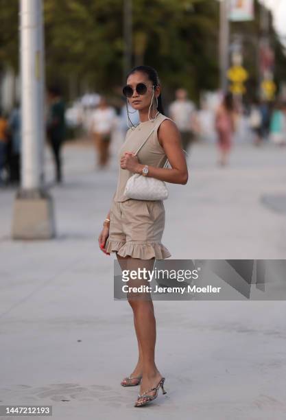Guest seen wearing a beige minidress, white Bottega Veneta bag, Chanel dark shades, a goldenwatch by Rolex on December 03, 2022 in Miami, Florida.