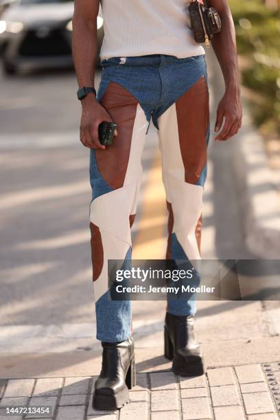 Guest seen wearing a cap, shades, a white tank top, patterned jeans and black plateau boots on December 03, 2022 in Miami, Florida.