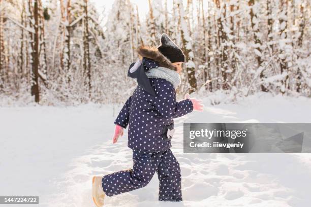 glückliches mädchen in jacke und hut spielen und spaß haben im winterwald. kind rennt und bewegt sich. glückliche kindheit. winterurlaub. tiefschnee. mädchen. warme kleidung - european sports pictures of the month december stock-fotos und bilder