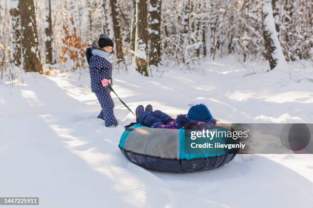 tobogganing and sledding. child play and have fun with sledge in winter forest. running and moving. happy childhood. winter holiday. deep snow. girls. warm clothes. tubing - frozen action stock pictures, royalty-free photos & images