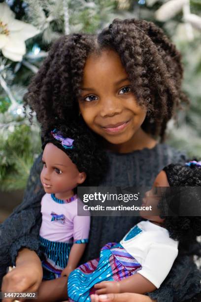 menina bonita que brinca com a boneca no cenário do natal. - little black dress - fotografias e filmes do acervo